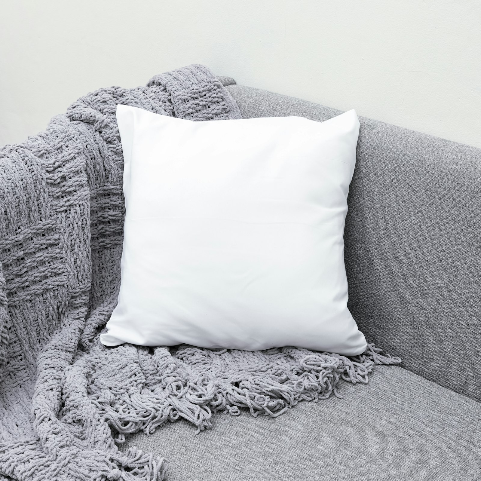 A white square cushion cover centred on a grey sofa