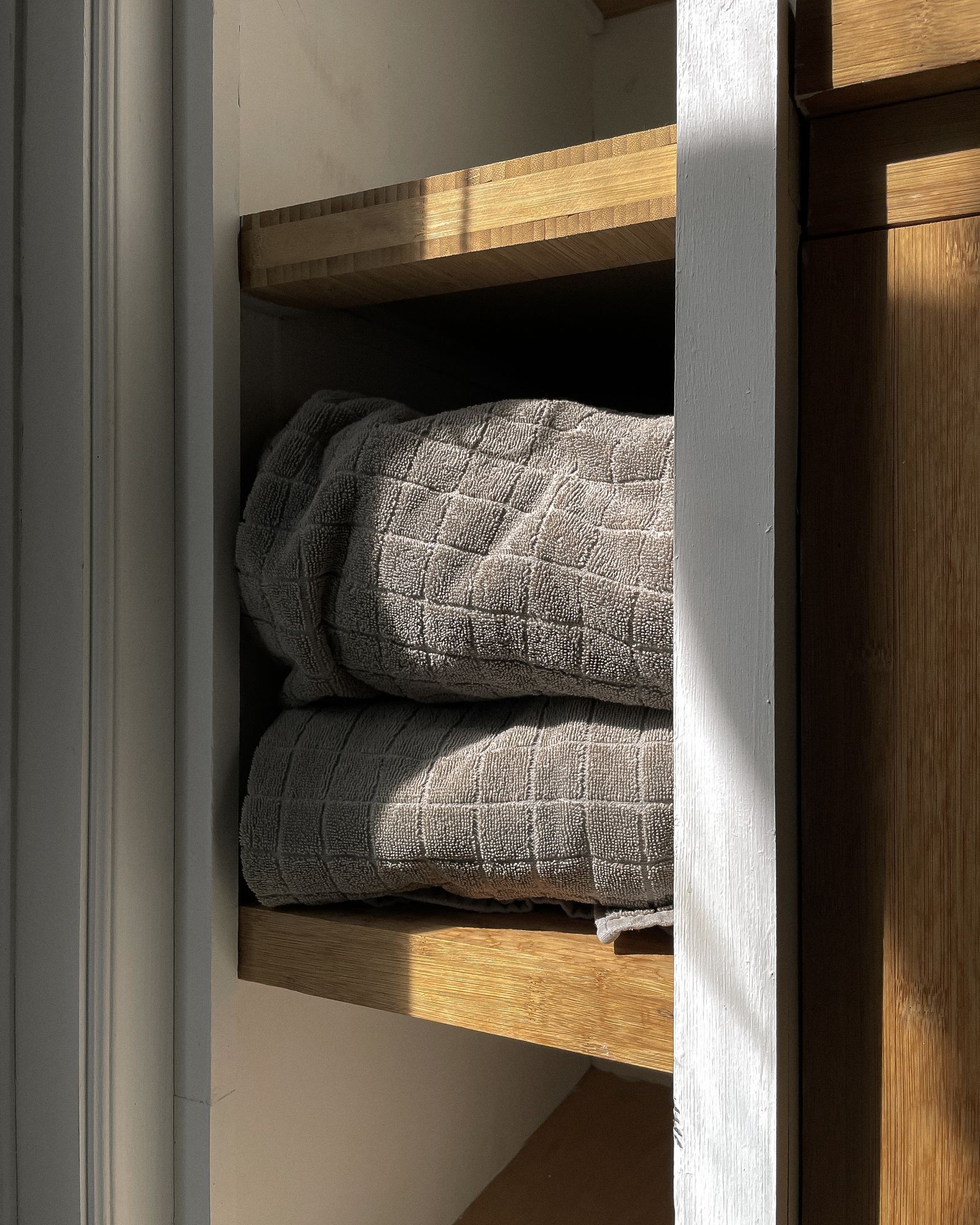 Folded waffle-weave cloth on a sunlit wooden shelf